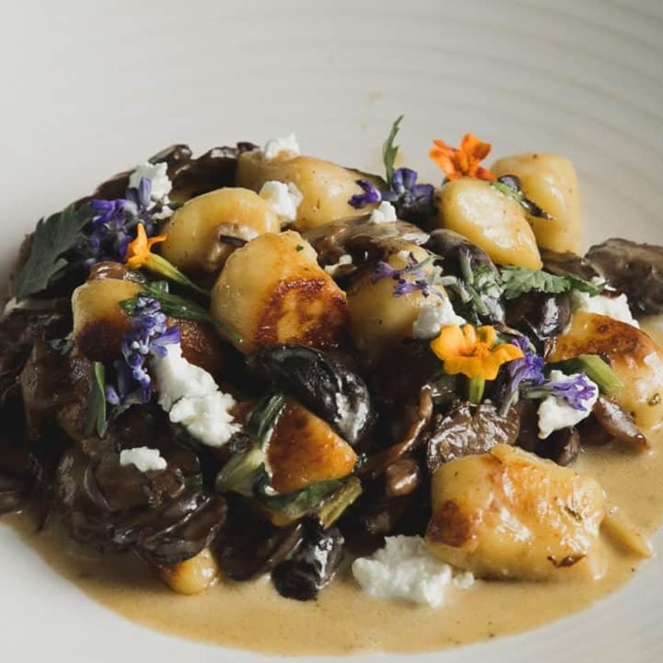 Gnocchi with mushrooms, feta, and edible flowers in a creamy sauce on a white plate.