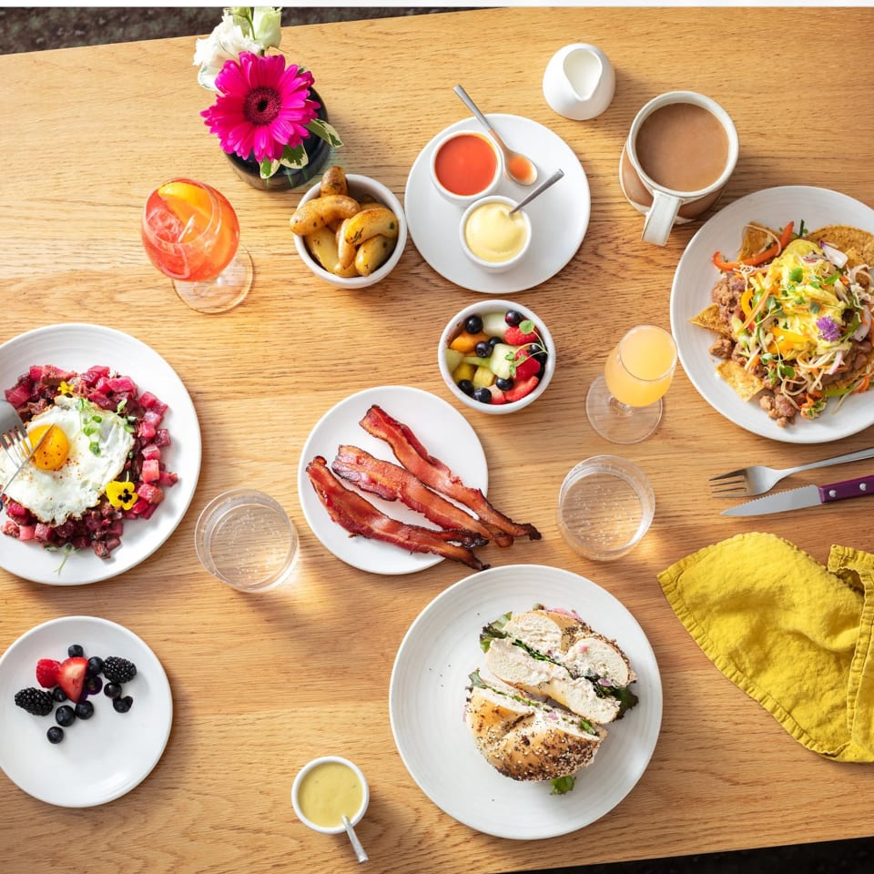 Overhead view of a wooden table set with various breakfast and brunch dishes, drinks, and a person eating.
