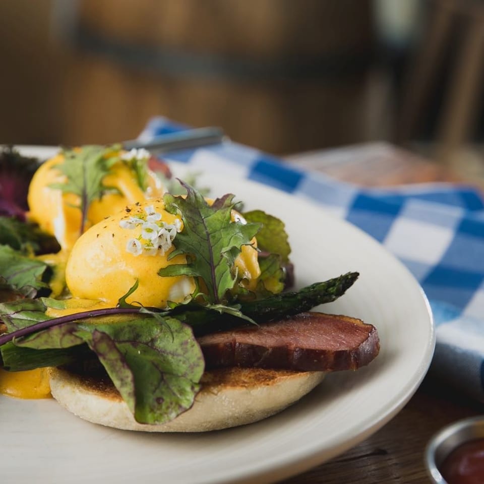 Eggs Benedict with roasted potatoes, bacon, asparagus, and greens on a white plate.